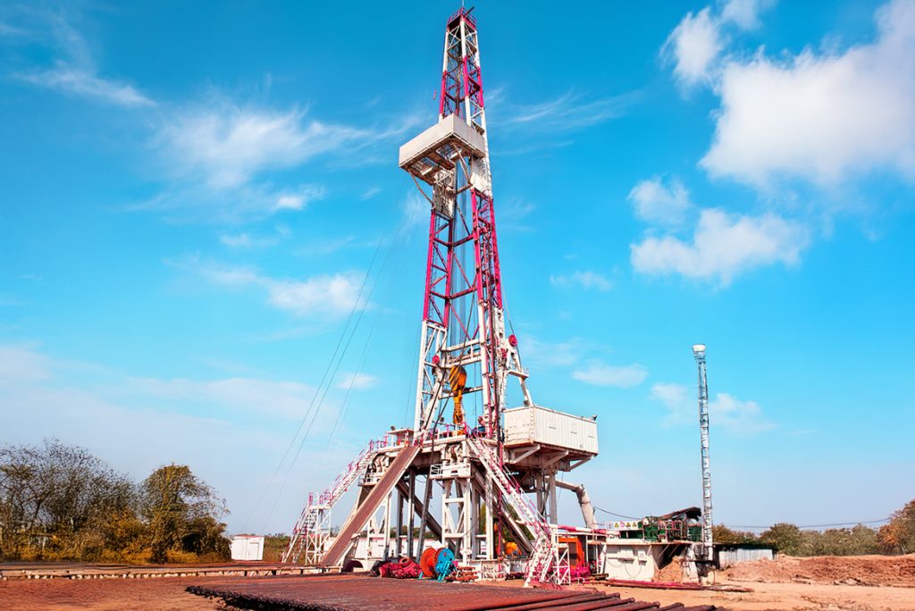 View of an oil derrick with steel scaffolding, lifting gear and a long pipe string that is guided vertically into the borehole.