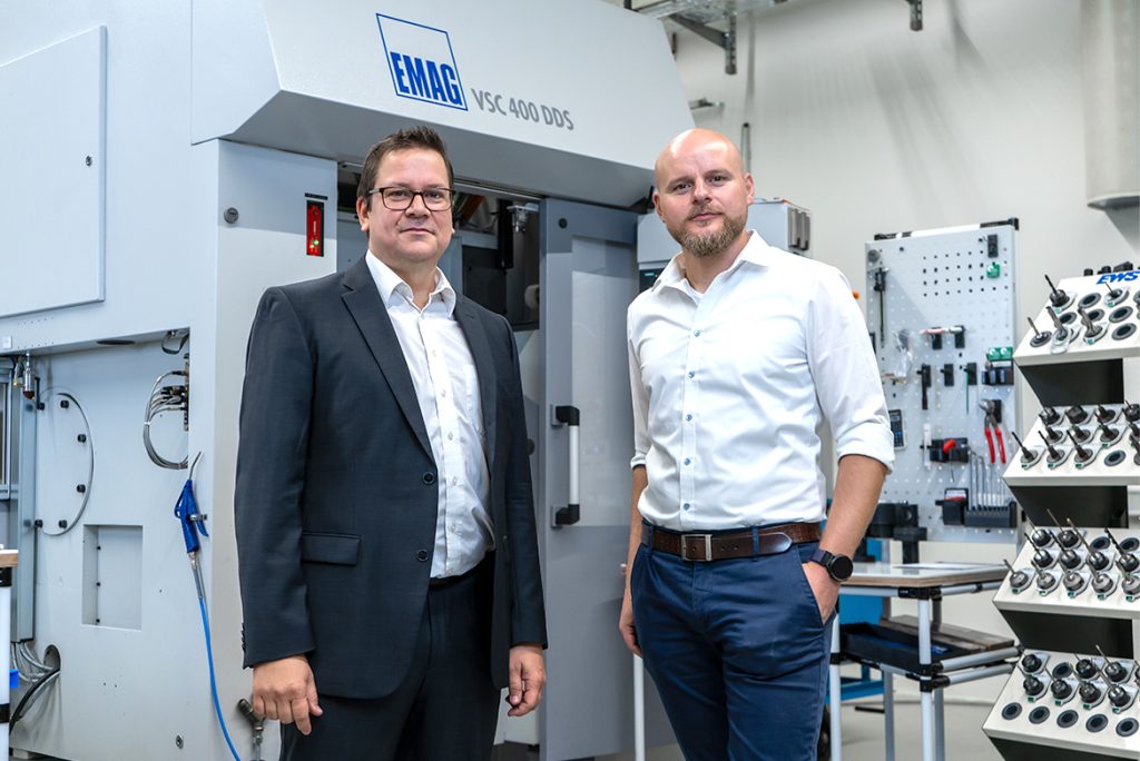 Oliver Hagenlocher (left) and Christian Schurr (right) stand in front of the VSC 400 DDS at EWS. The topic is retrofitting for precision hard machining of tapers and gears. 