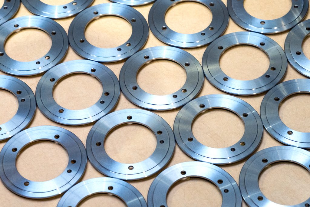 Reihen von gleichmäßig angeordneten, präzise bearbeiteten, ringförmigen Metallteilen auf heller Unterlage, fertig für die Auslieferung an die Automobilindustrie.